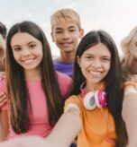 Portrait of smiling multiracial teenage friends taking selfie, looking at camera on urban street. Young influencer recording video standing together with friends. Summer concept
